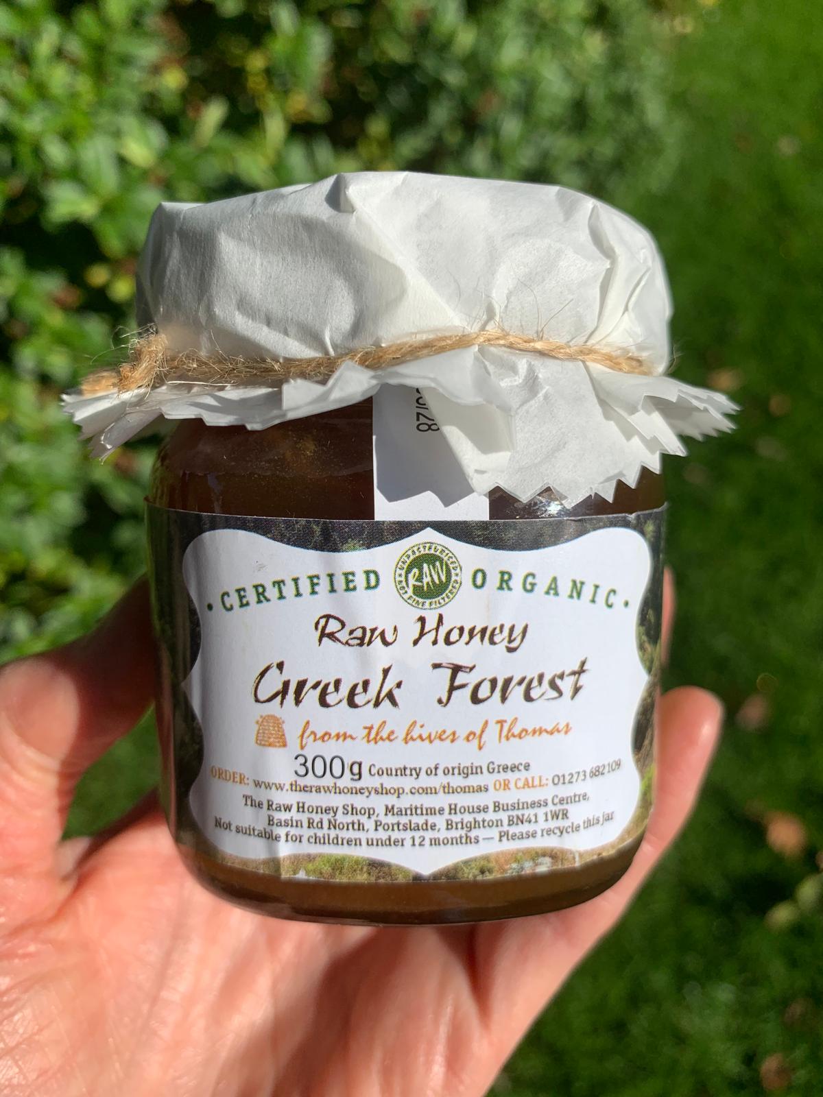 Hand holding a jar of honey with white label to the front with the words raw honey forest honey